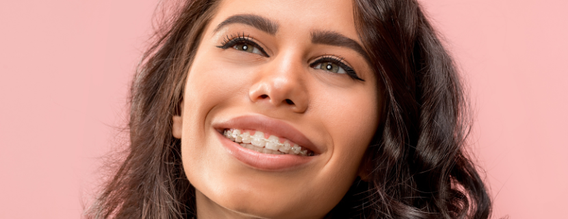 close of up beautiful woman with brown curly hair smiling into the distance, wearing clear wired braces 