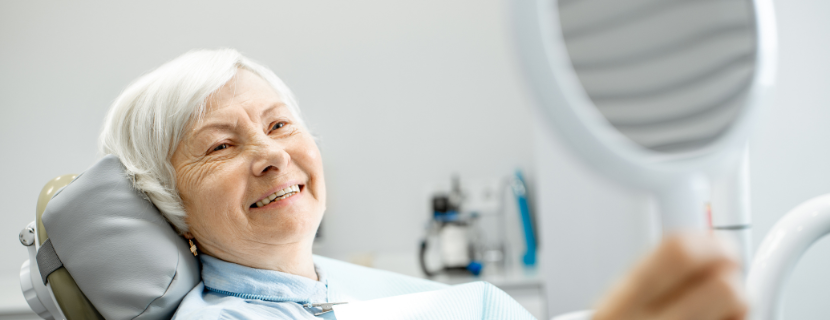 An older lady smiling into a handheld mirror at her new full smile after dental implants