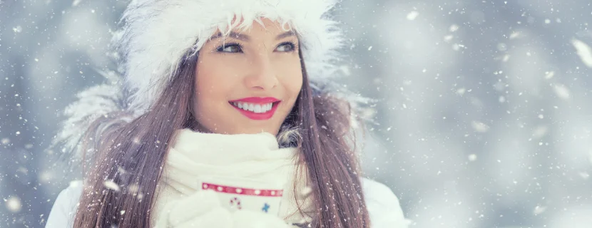 Transform your smile this winter woman standing in the snow with bright, white teeth and red lipstick, dressed for winter