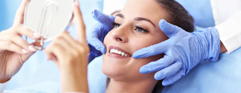 Woman smiling into mirror on dental chair whilst dentist points at her white straight smile